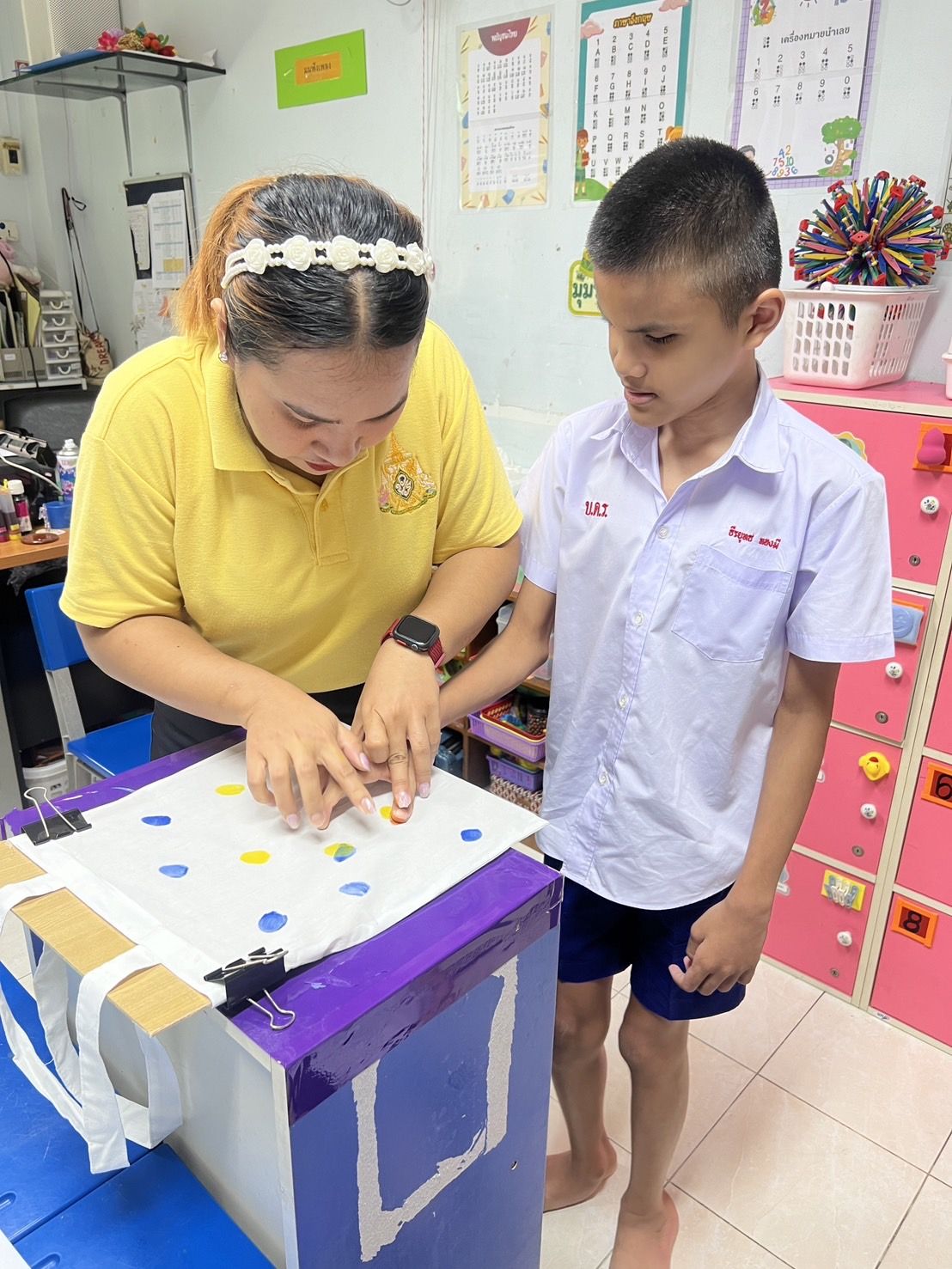 ครูจับมือนักเรียนพิมพ์ลายบนกระเป๋าผ้า